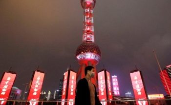 A man wearing a face mask walks past the Oriental Pearl Tower lit with messages reading "Stay strong China", on the Lantern Festival, which marks the end of the Chinese Lunar New Year celebrations, following an outbreak of the novel coronavirus in the country, in Shanghai, China February 8, 2020. Picture taken February 8, 2020. cnsphoto via REUTERS   ATTENTION EDITORS - THIS IMAGE WAS PROVIDED BY A THIRD PARTY. CHINA OUT.