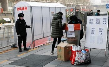 A security guard stands outside a plastic tent set up to disinfect people coming in at the entrance of a residential compound, as the country is hit by an outbreak of the new coronavirus, in Beijing, China February 13, 2020. The placard at the entrance of the tent reads, "Disinfection tunnel". REUTERS/Carlos Garcia Rawlins