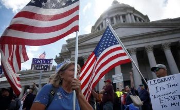 People hold signs and American flags as hundreds protest against the state's extended stay-at-home order to help slow the spread of the coronavirus disease (COVID-19) at the Capitol building in Olympia, Washington, U.S. April 19, 2020. REUTERS/Lindsey Wasson