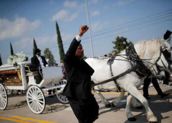 A mourner raises his arm as the horse-drawn carriage carrying the casket containing the body of George Floyd, whose death in Minneapolis police custody has sparked nationwide protests against racial inequality, travels to Houston Memorial Gardens cemetery in Pearland, Texas, U.S., June 9, 2020. REUTERS/Carlos Barria